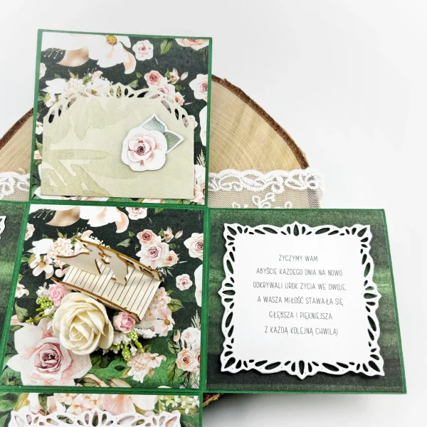 Ręcznie robiony exploding box ślubny z figurką pary młodej i kwiatową kompozycją w kolorze butelkowej zieleni z różowymi dodatkami.